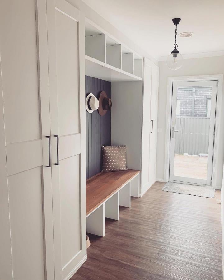 Light gray built-in mudroom seating area with navy beadboard back from @home.sheridan featuring wood bench and storage cubbies.