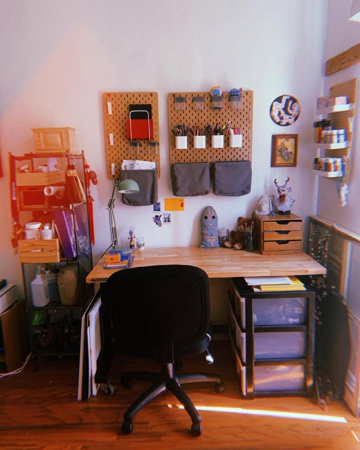Natural wood pegboard wall with grey pouches and white containers in cozy home office setup by @janell.draws showing ikea office pegboard ideas for organized workspaces
