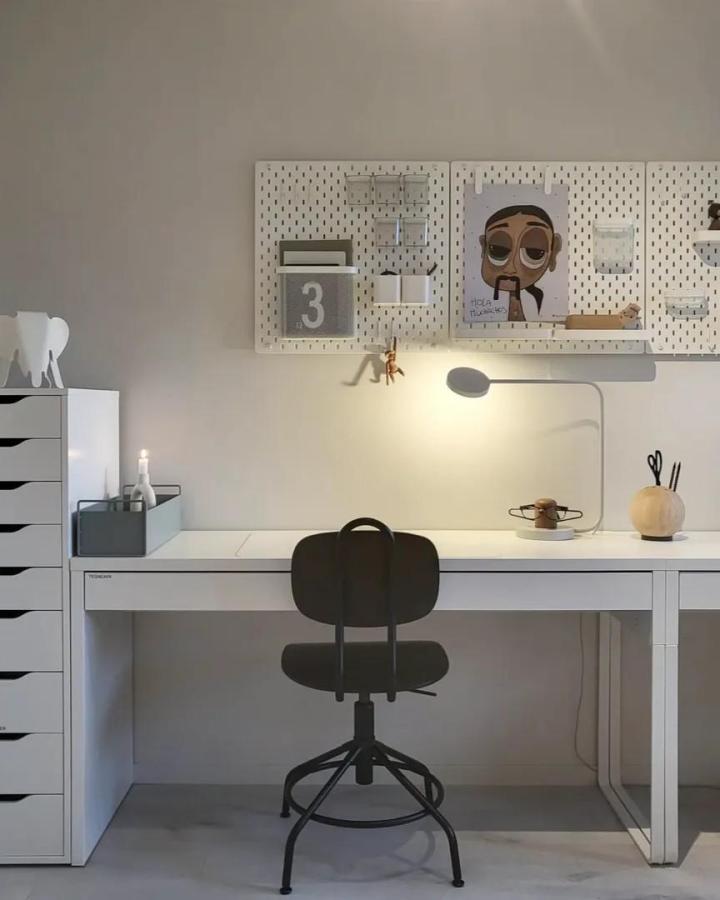 White minimalist pegboard wall with clear containers and hooks above a white desk from @maa1983. Modern, tidy workspace with small decor and lighting.