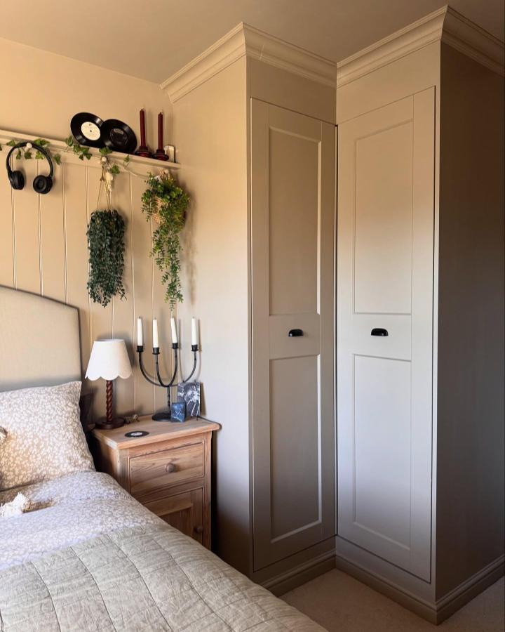 Beige shaker style Ikea PAX corner wardrobe ideas from @mabelinthehouse with black handles and crown molding in a cozy bedroom corner.