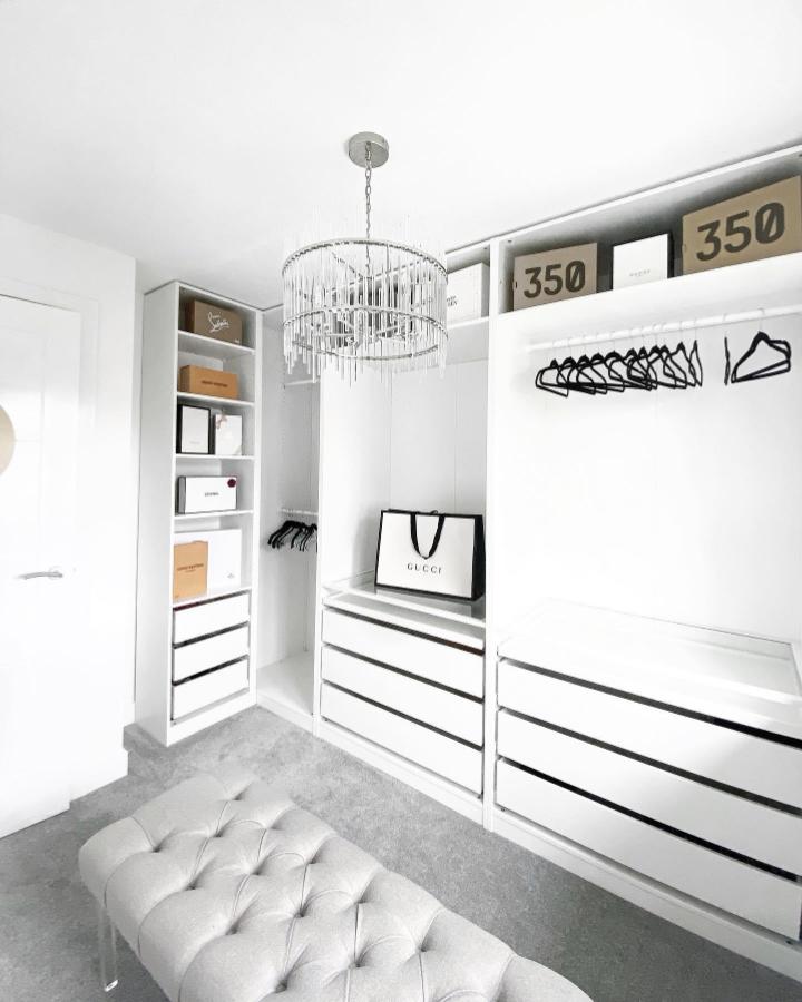 White minimalist wardrobe corner from @weir_home with drawers, open shelves, black hangers, and tufted bench seating.