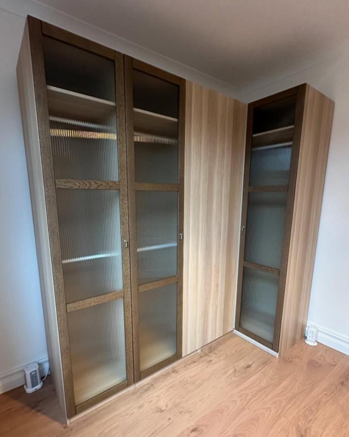 Fluted glass and warm walnut framed corner wardrobe by @flatpackprofessionals with light oak panels creating modern rustic storage.