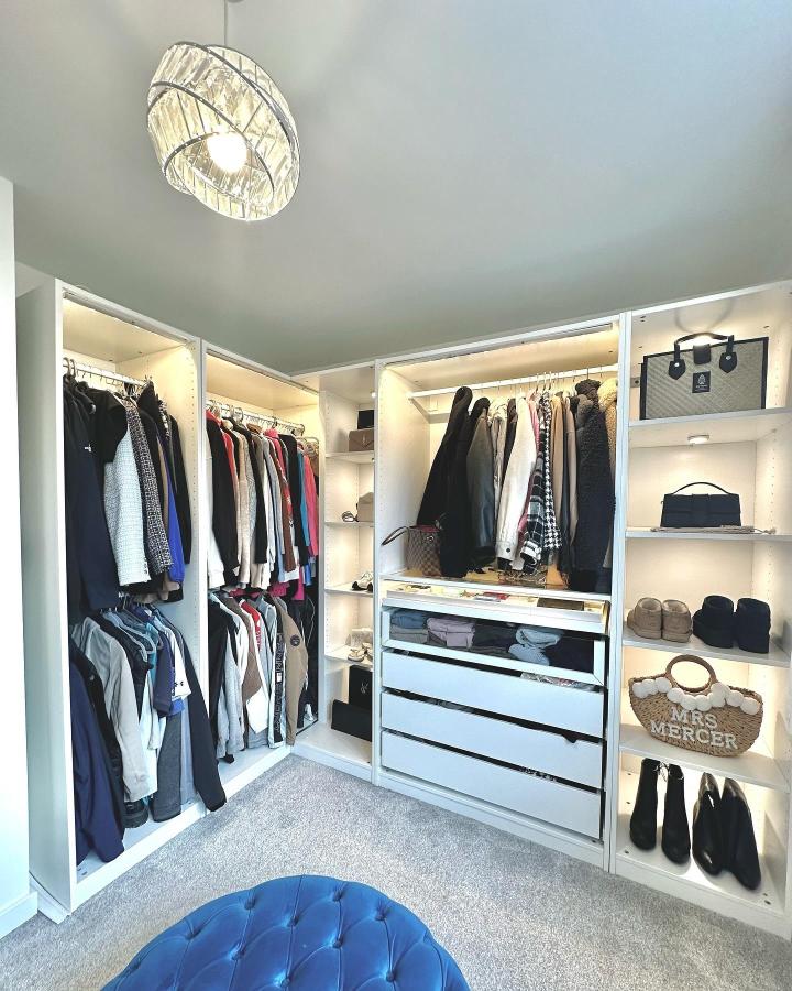 Bright white modular wardrobe with built-in lighting from @athomewithkirsty_ featuring organized clothing and accessories in a corner closet setup.
