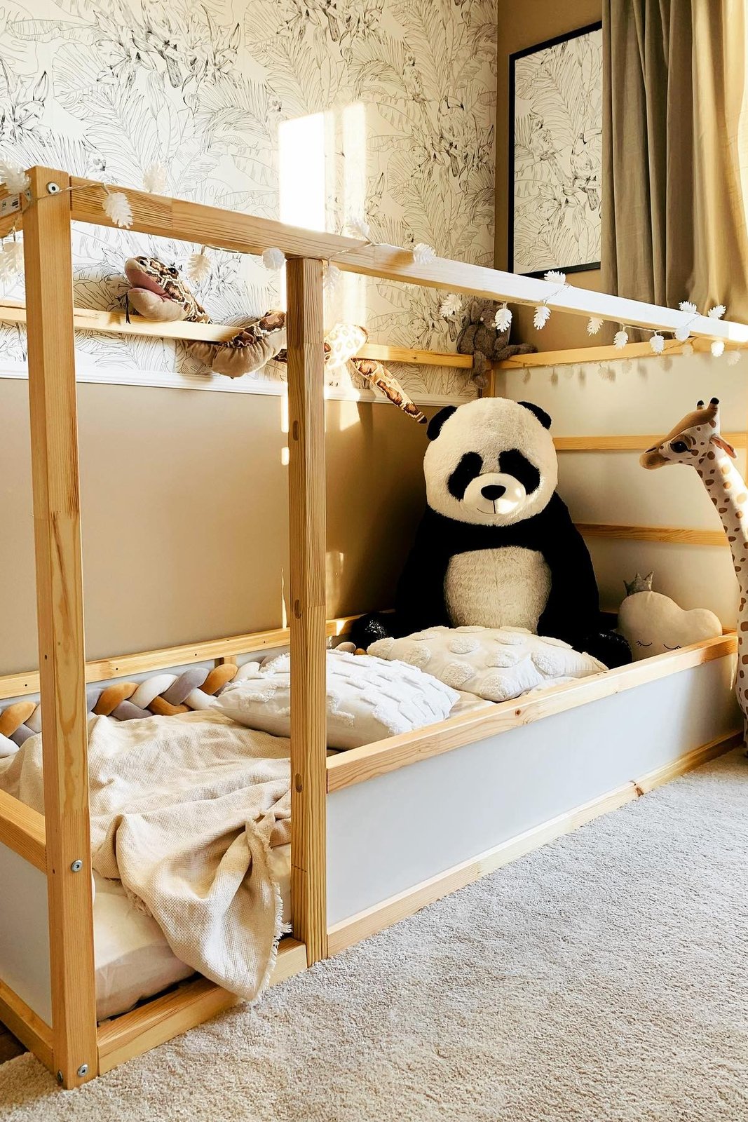 Cozy IKEA KURA bed with fairy lights, soft bedding, plush toys, and natural wood framing