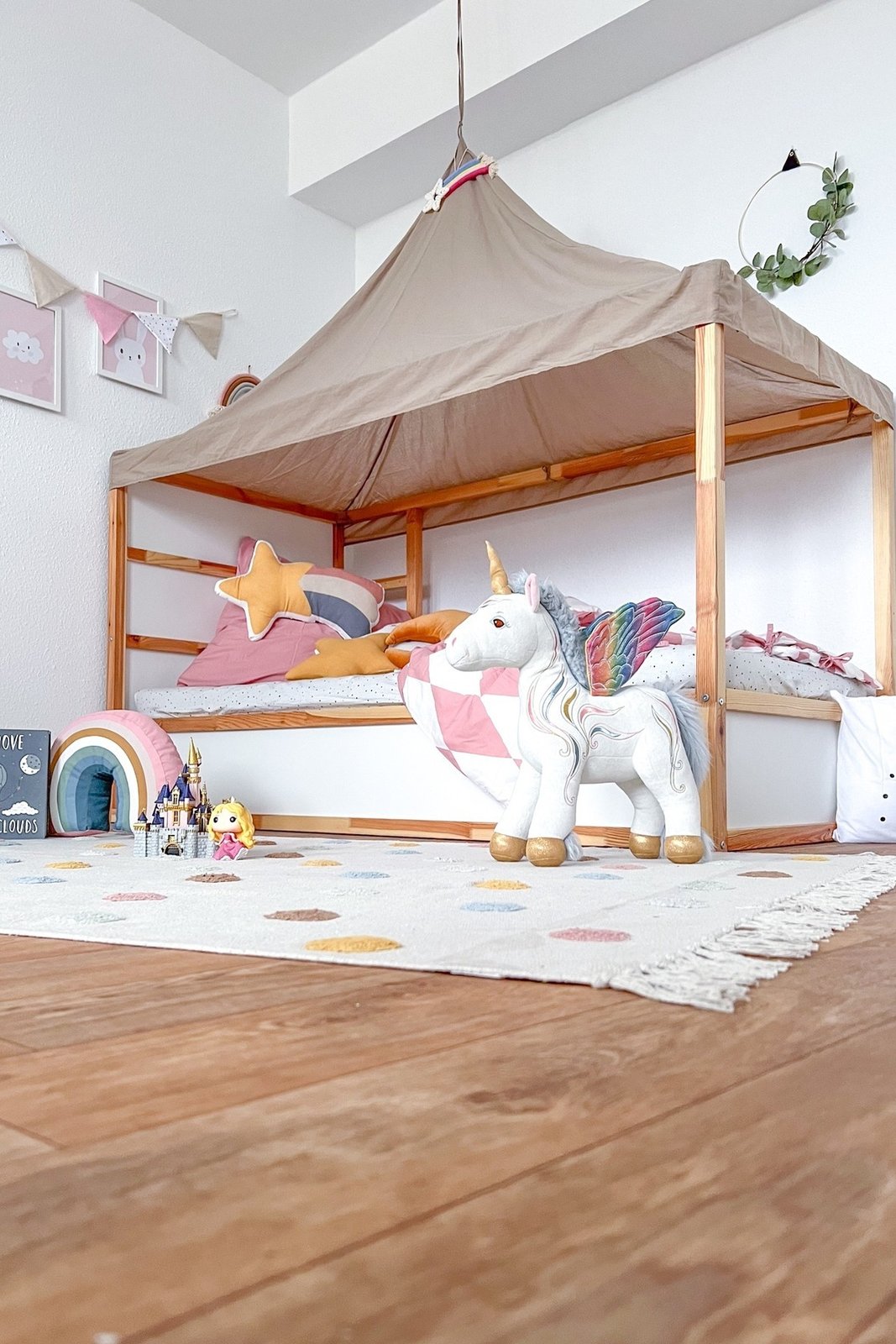 Soft canopy-covered KURA bed with colorful bedding, plush unicorn, playful rug, and charming bedroom accessories
