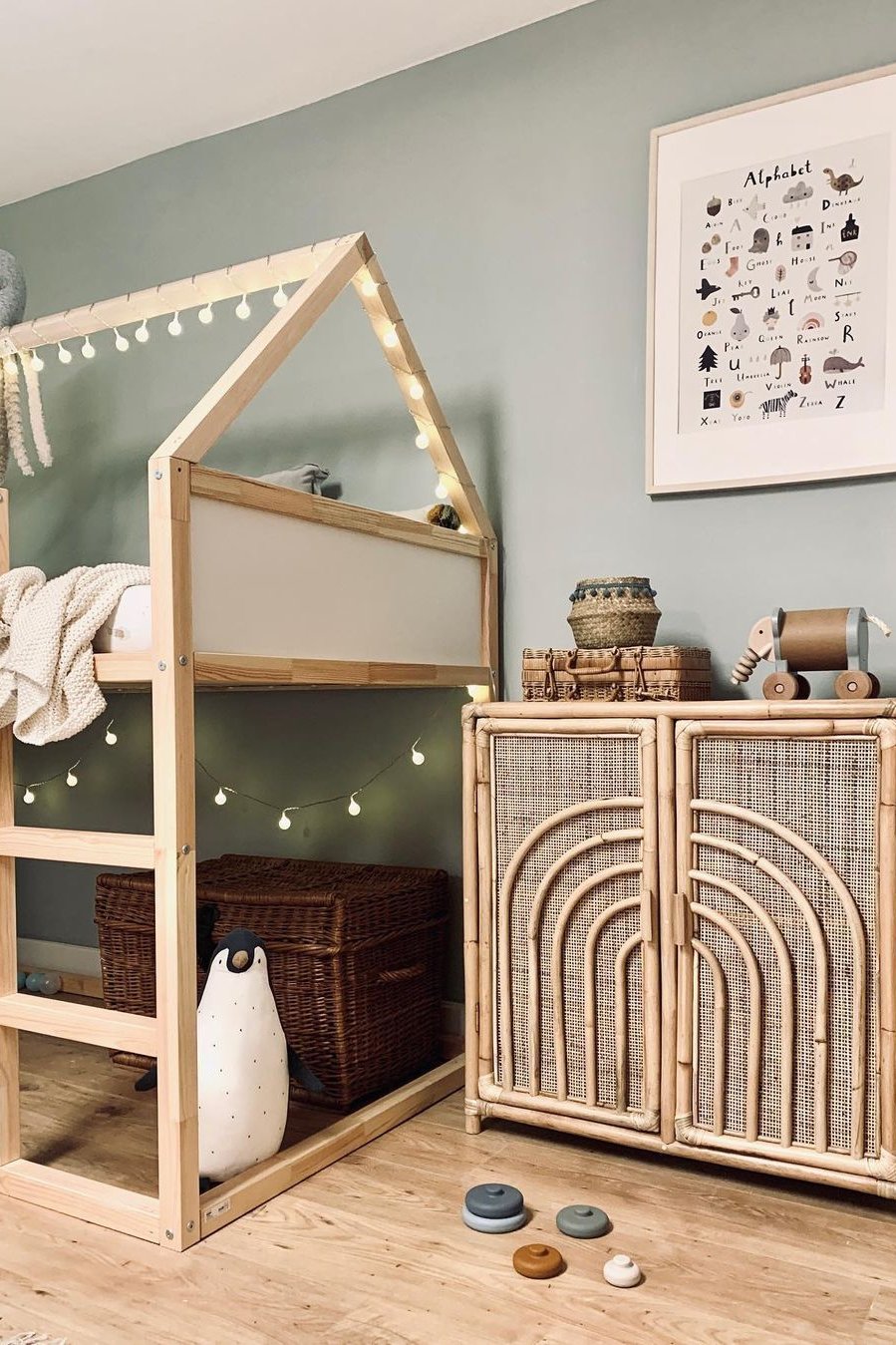 Natural wood Kura bed with house frame, string lights, woven baskets, and cozy child-friendly accessories