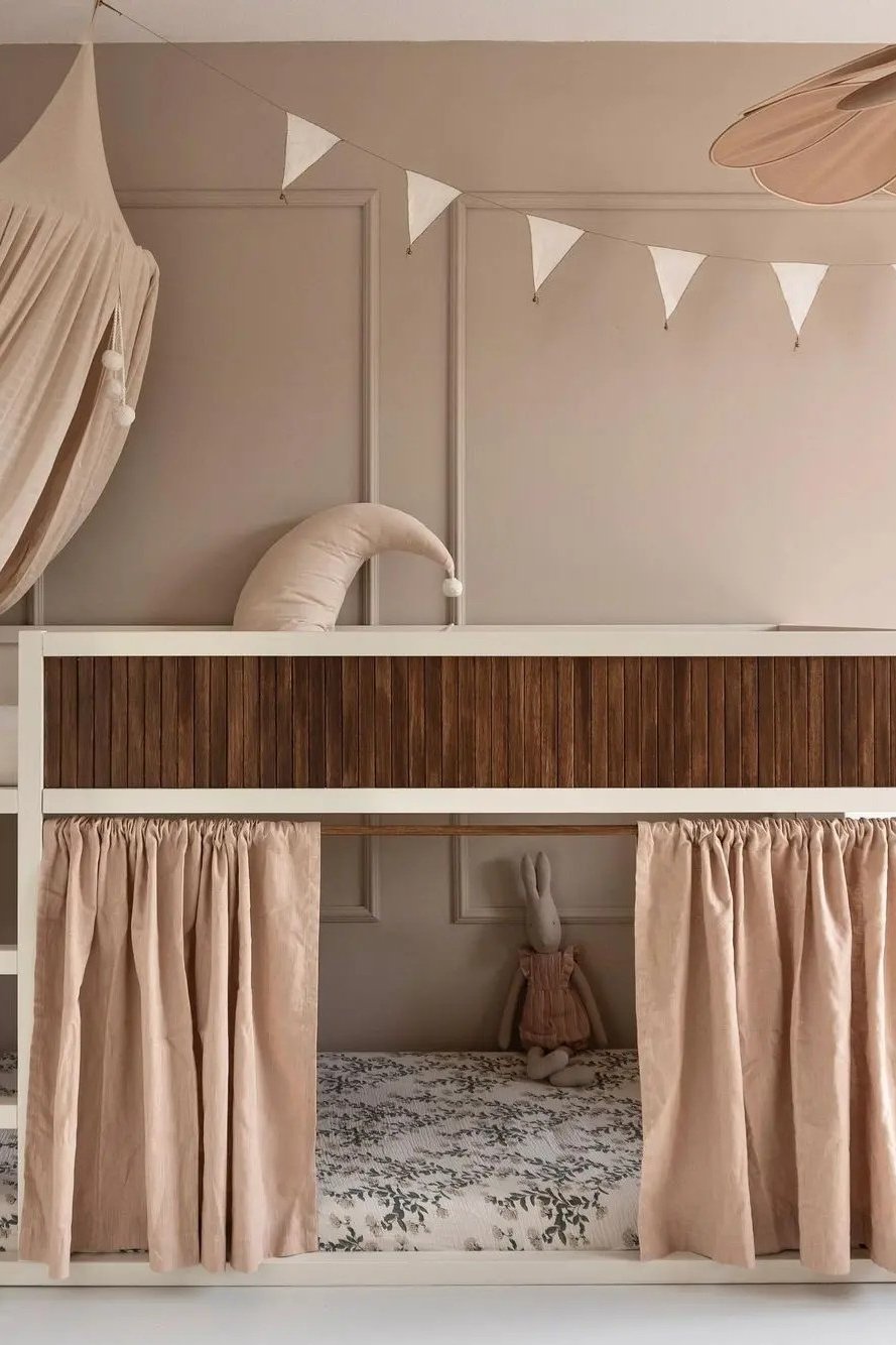 Kura bed with under-bed curtains, decorative wooden side panel, floral bedding, and soft nursery accents