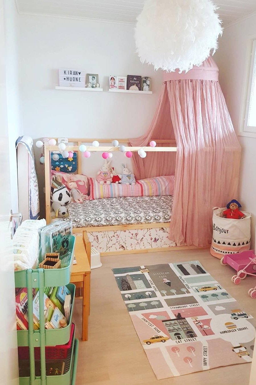 Pink KURA bed canopy with pom-pom lights and playful bedding, showcasing charming accessories for a child’s bedroom