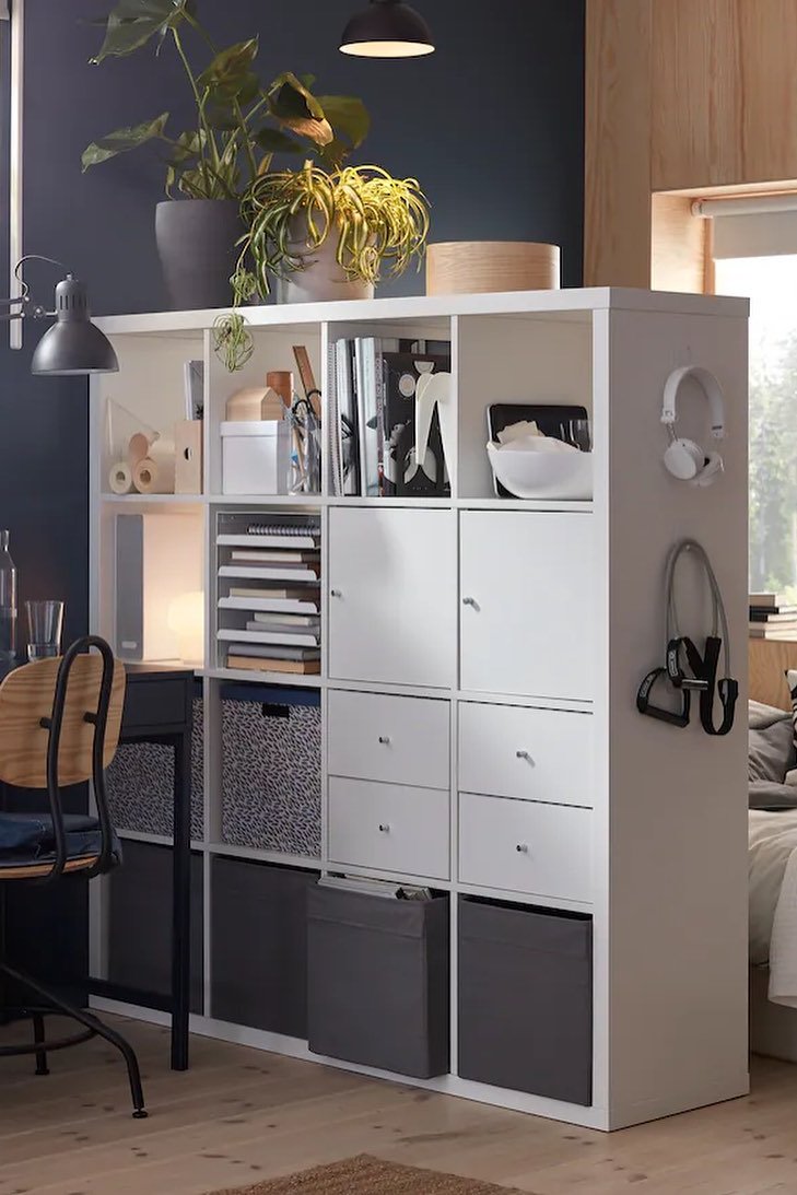 IKEA KALLAX divider with open shelving and storage inserts separating a workspace and bedroom