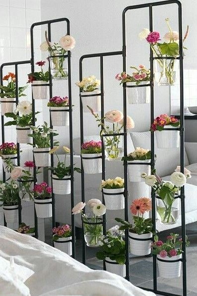 Black IKEA plant stand with white pots and flowers used as a stylish bedroom space divider