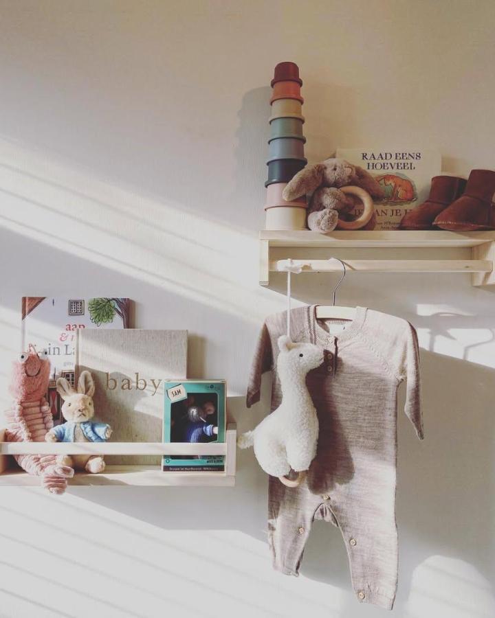 Beige wooden shelves in a cozy nursery styled by @homestylinginspiration holding plush toys and pastel stacking cups.