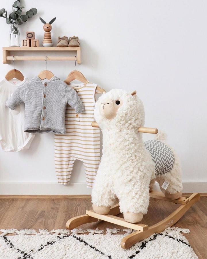 Natural wood nursery shelf with baby clothes and plush rocking toy from @ourhillhome. Cozy, minimal, and playful baby space.