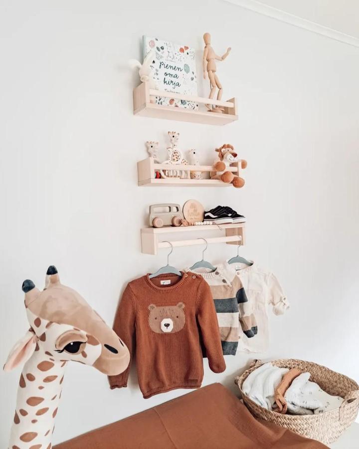 Light natural wood wall shelves and hanging rod nursery storage from @annikilkki with cozy toys and baby clothes display.