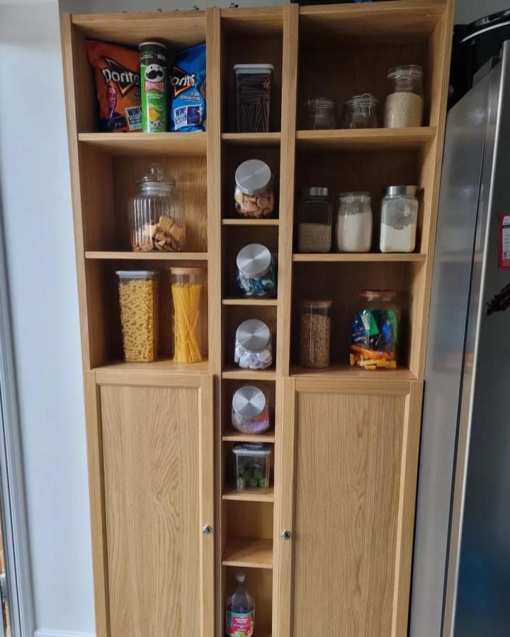 Natural oak pantry with slim vertical jars and mixed open closed storage by @windermere_no37. Bright and organized kitchen storage solution.