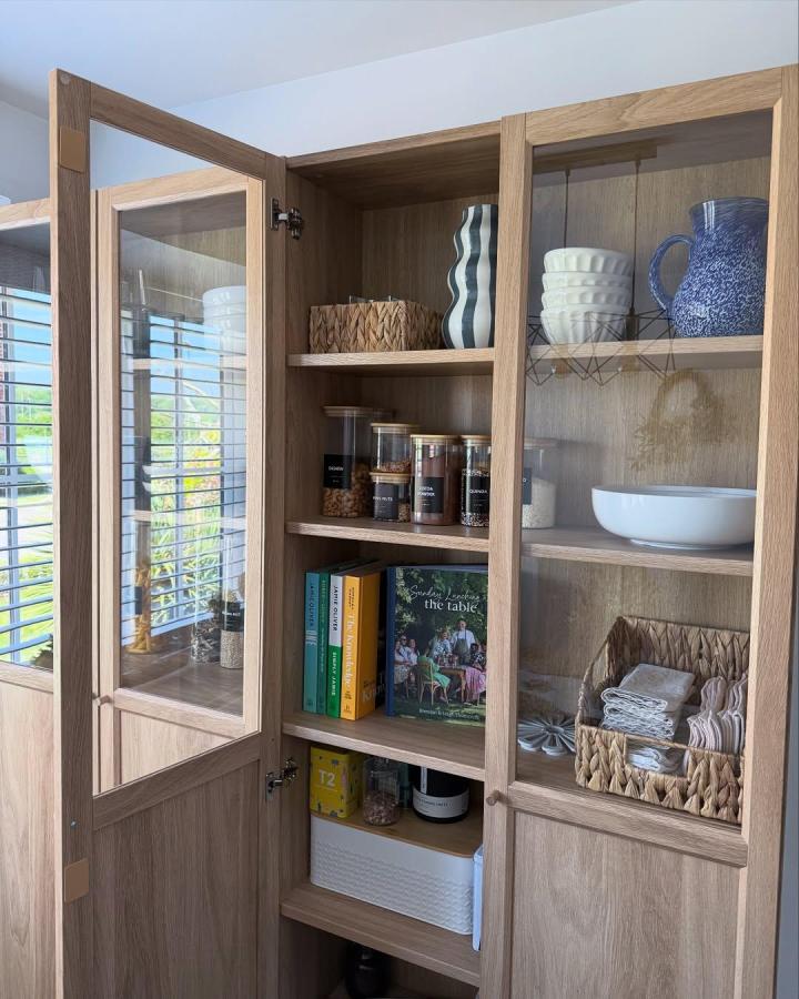 Light oak wood and glass door pantry cabinet from @housetohomewithemma with mixed texture storage and neat kitchen organization.