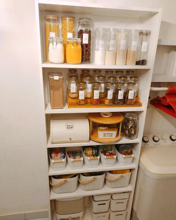 Clear glass jars and white baskets with wooden handles in a neat pantry from @teratak_fs organized for kitchen essentials and dry goods storage.