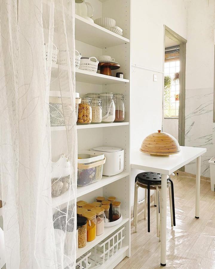 White minimalist pantry shelving with sheer curtain and natural accents from @rumah.sara Bright, organized storage with glass jars and woven baskets in soft lighting.