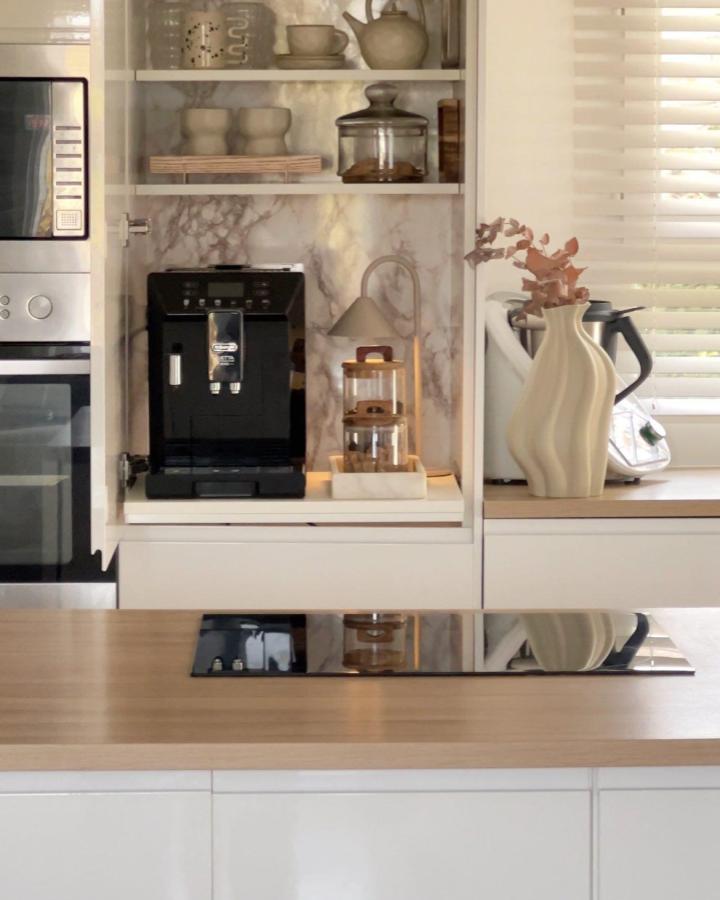 Cream and white hidden coffee station with marble backsplash and pull-out shelf from @interiorym featuring espresso machine and wood accents.