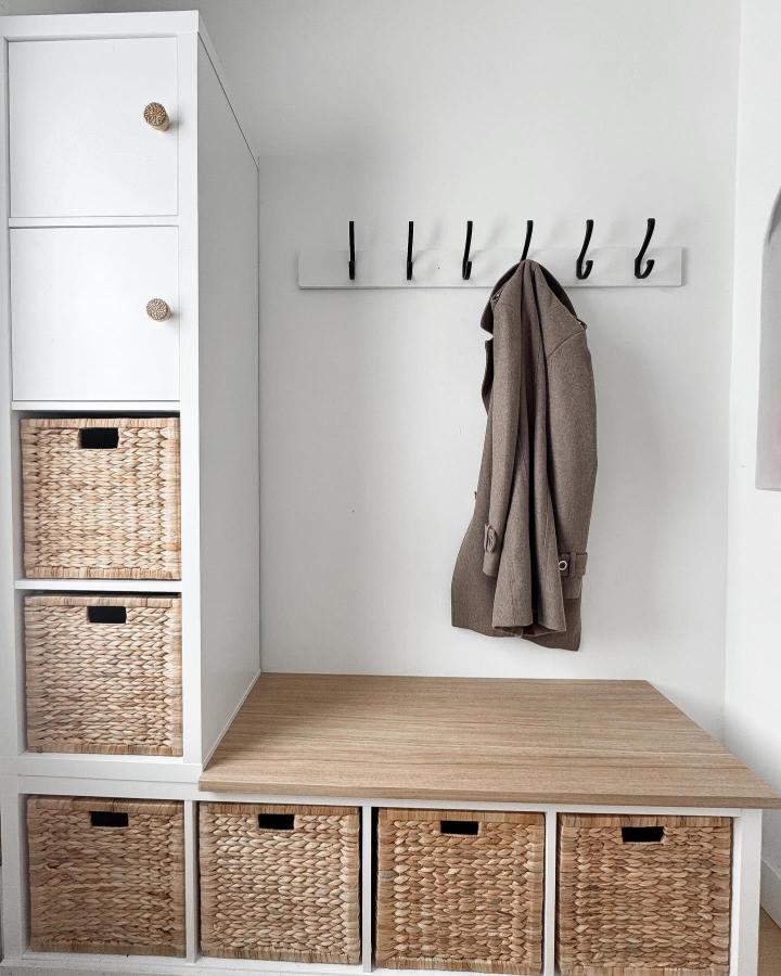 White and natural woven basket storage bench with black hooks in minimalist home entry by @jghalebxo. Inviting practical and stylish storage solution.