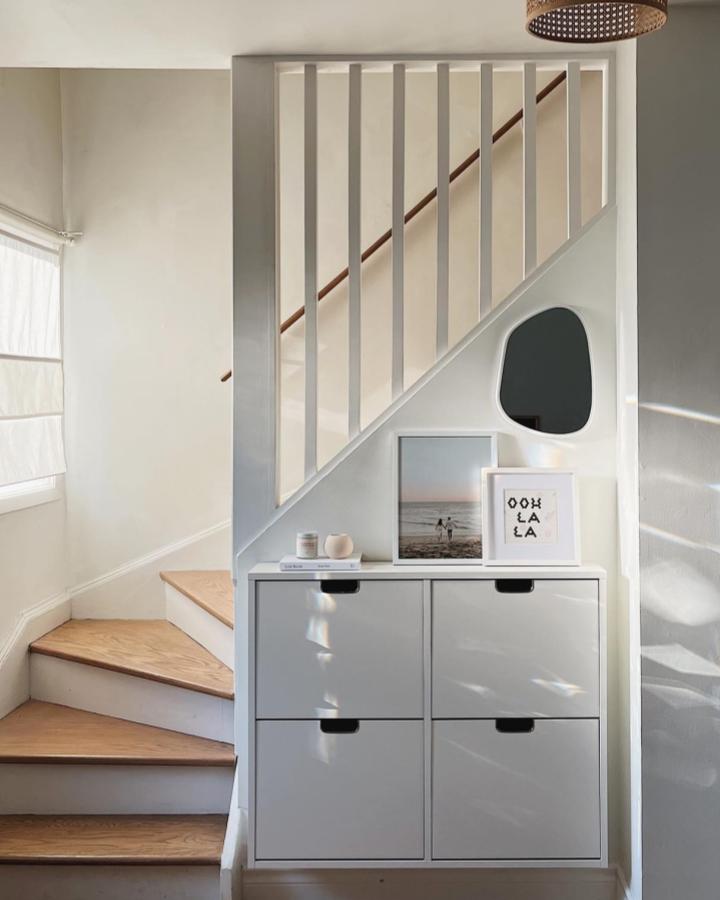 White minimalist STÄLL shoe cabinet under stairs by @wonhaus with mirror and artwork in cozy home entry nook