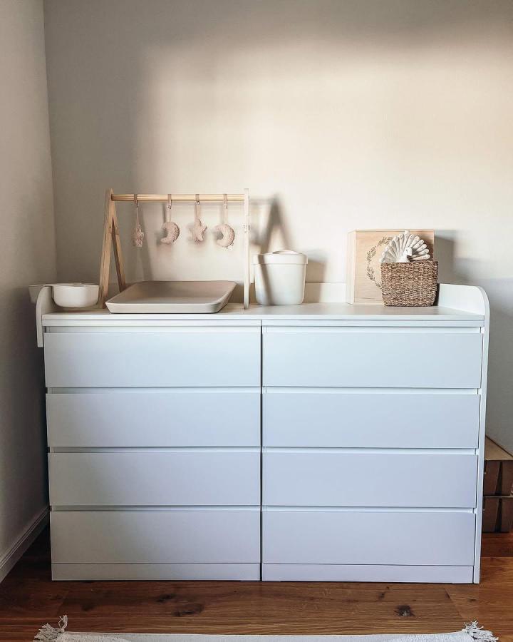 White minimalist dresser with natural wood baby gym and baskets from @schreinerei_linker styled for a cozy baby room.