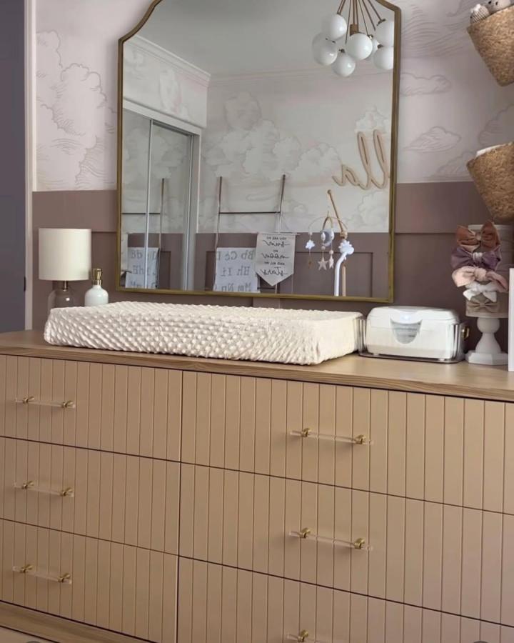 Beige textured dresser with brass handles in nursery from @themartinezcasita styled with soft changing pad and vintage mirror.