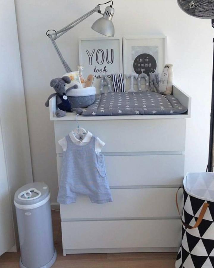 Gray cushioned changing station on white dresser by @servicesgoup with soft toys and minimalist decor in nursery corner.
