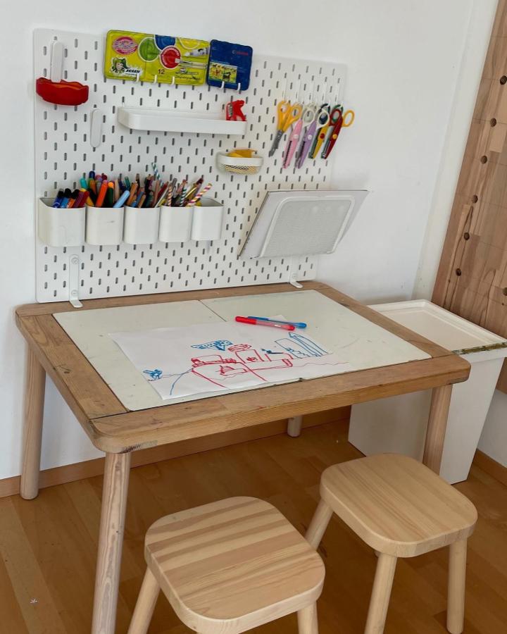 Natural wood FLISAT table and stools with white Ikea Skådis pegboard and TROFAST storage from @wildewichtel showcasing ikea montessori playroom ideas organization.