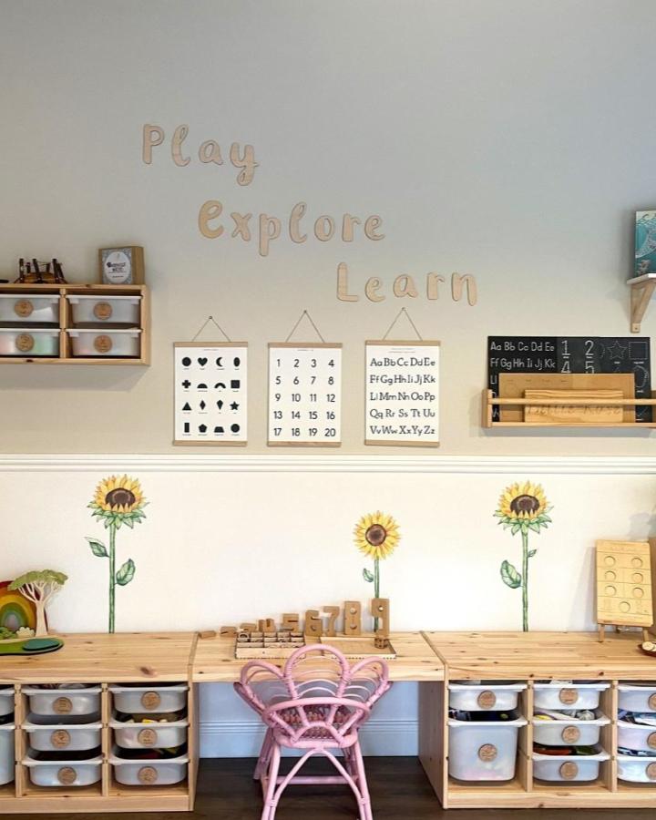 Natural wood and clear plastic IKEA TROFAST storage with pastel pink chair and sunflower decals by @cocreative_design Montessori-style kids area.