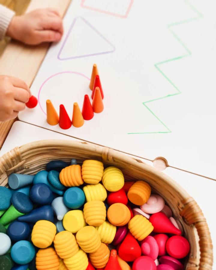 Bright wooden cones and discs on a natural wood Ikea FLISAT table from @ourdreamplayroom in a kids learning activity setup.