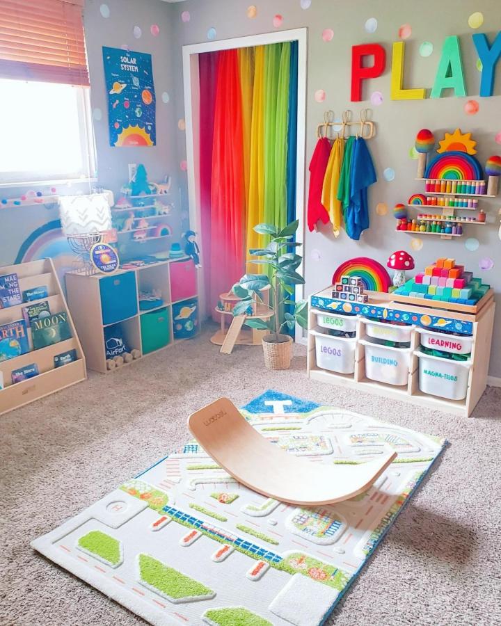 Rainbow curtain and pastel dotted walls in child’s playroom with natural wood toys and IKEA TROFAST storage by @chaos.and.rainbows a colorful, organized space promoting independent play.