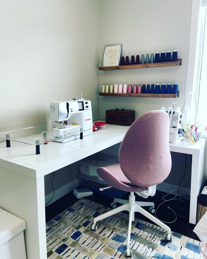 Pink Hattefjäll chair and white Malm Desk sewing workspace from @sewinginmycloset with colorful thread cones on wooden shelves ikea sewing table ideas.