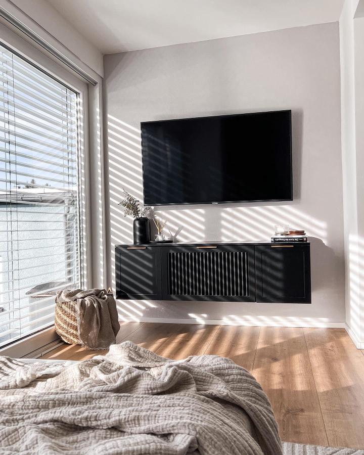 Black floating media console in minimalist living room by @maxis.homestory featuring ikea small living room hacks with slatted cabinet doors and wall mounting.
