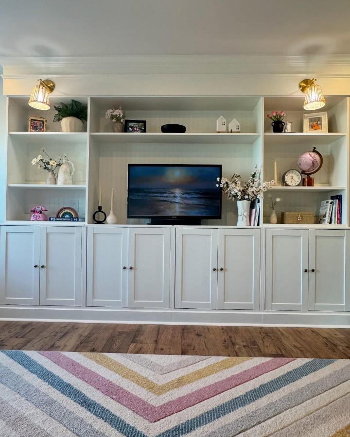 White built-in storage with open shelves and closed cabinets from @paisleyathome. Functional living room organization with stylish accents.
