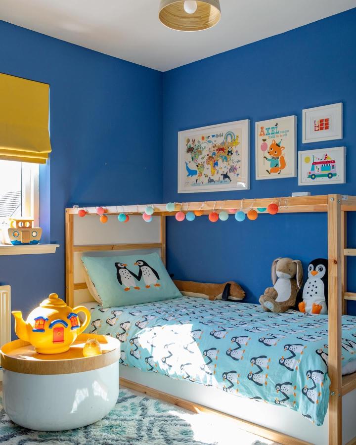 Blue-and-wood Kura loft bed from @fromcity2suburb. Pom-pom string lights brighten penguin bedding.