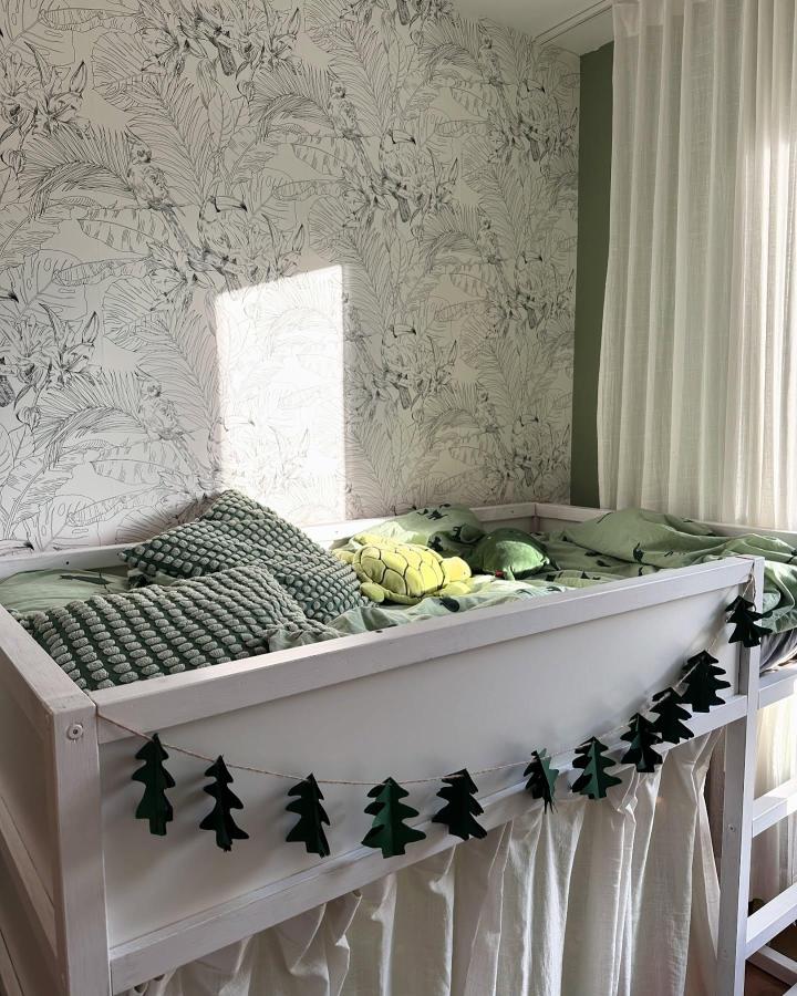 Soft white and forest green Ikea Kura bed from @dominika.byczek. Under-bed curtain and tree garland create a cozy woodland nook.