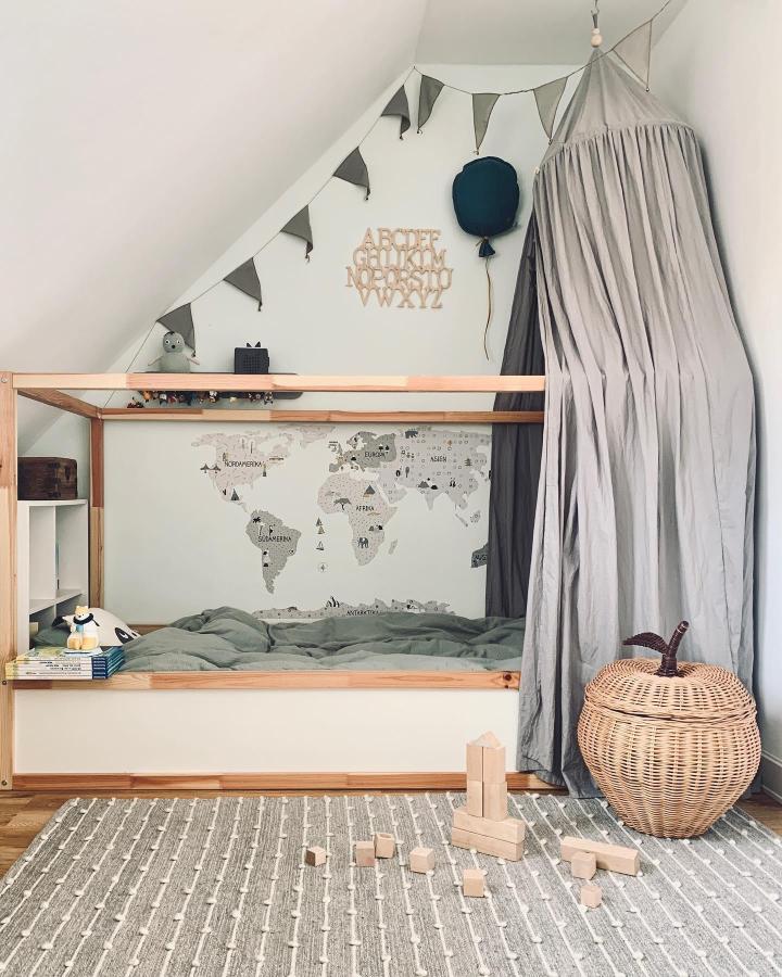 Grey canopy wooden KURA bed from @__mamalina__. Layered fabric, bunting, world map, and soft green bedding create a cosy hideaway.