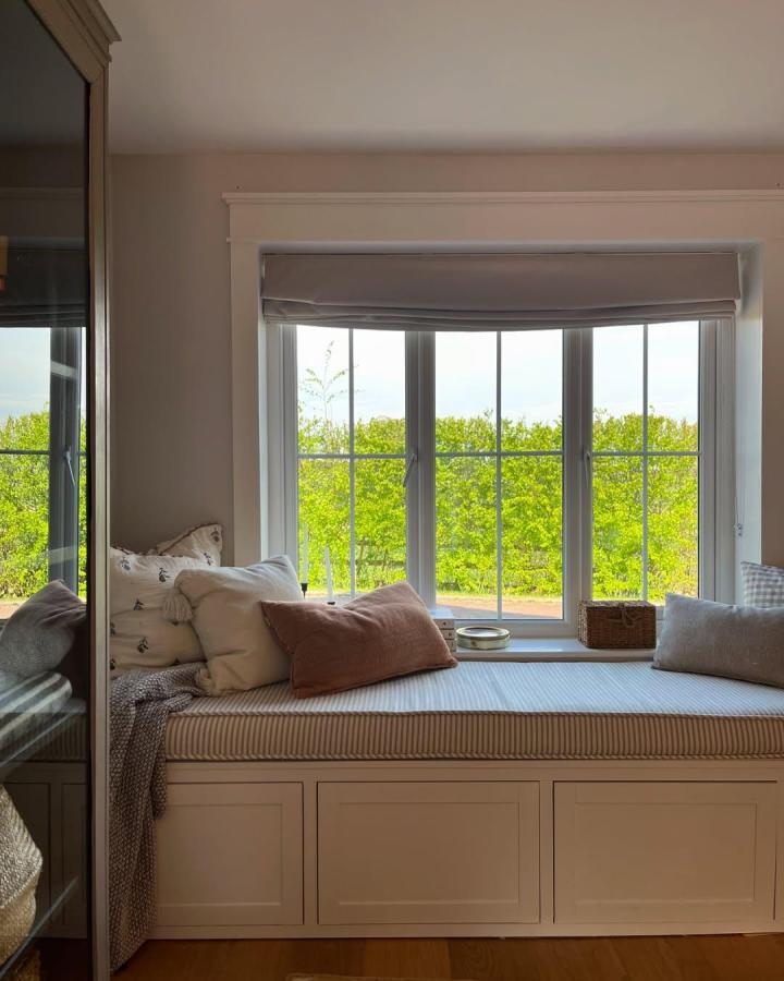 Warm greige window seat from @fourthhome_. Framed cabinetry, soft cushions, and garden views.
