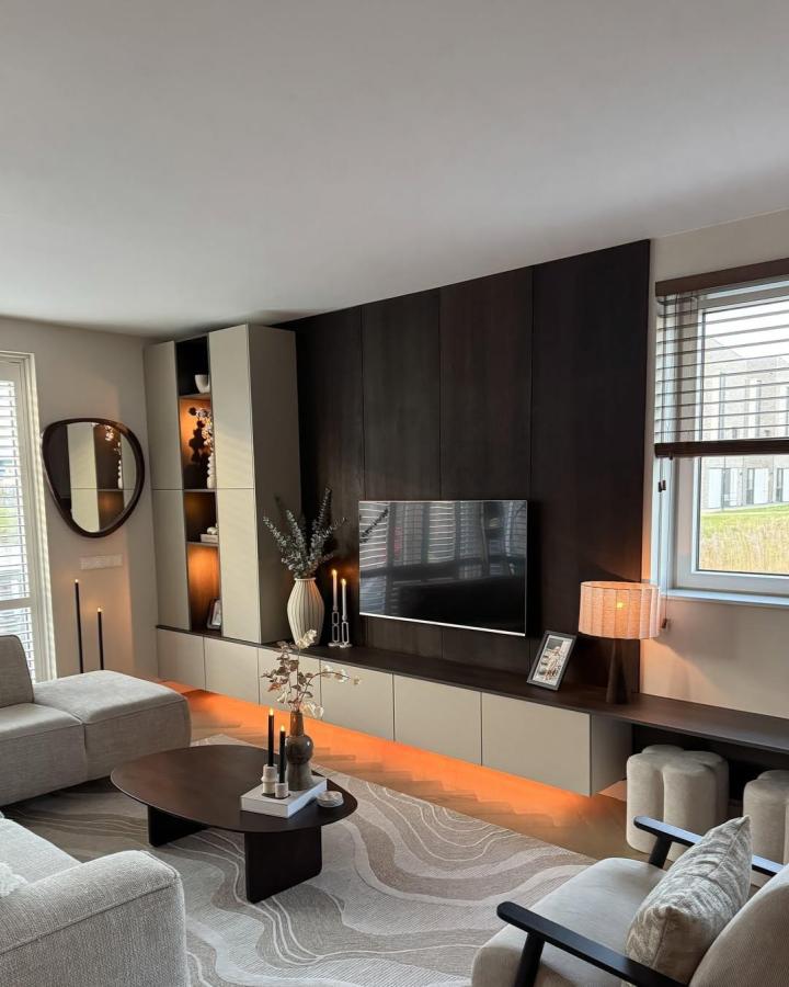 Dark walnut living room media wall from @huisjenr.33. Cream Besta cabinets, open shelving, and warm underlighting.