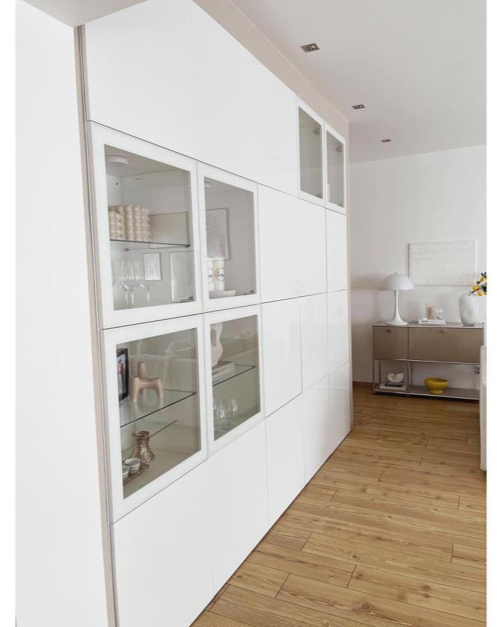 White glass-fronted living room storage from @interiorhoch4. Wall-to-wall Besta cabinetry displays decor.