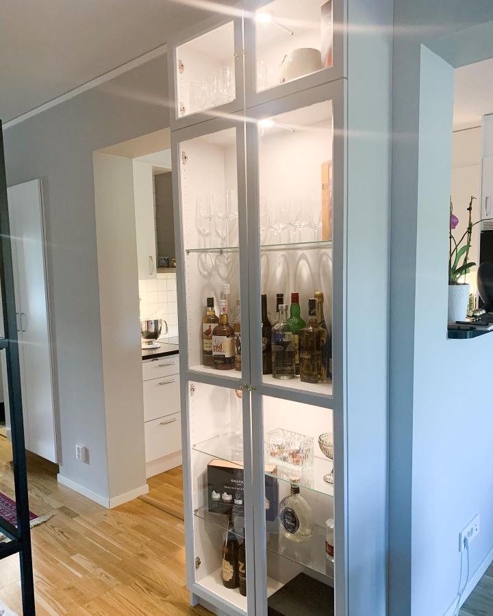 White glass-fronted bar cabinet from @jennyjontheblock. Partial room divider with bottles and stemware.