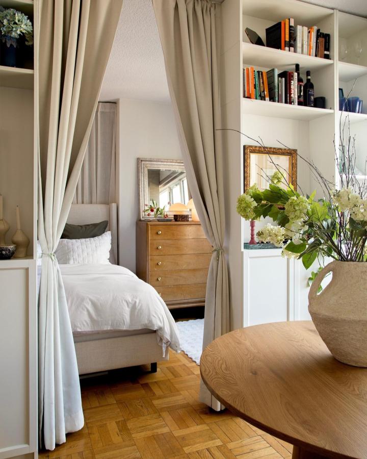 Creamy white Billy bookcase room divider from @kiritinbeyer. Beige curtains frame a cozy bedroom beside the living area.