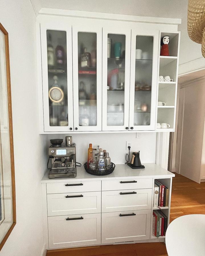 White glass-front coffee cabinet from @braveelement. IKEA Sektion nook with espresso machine and open cup shelves.
