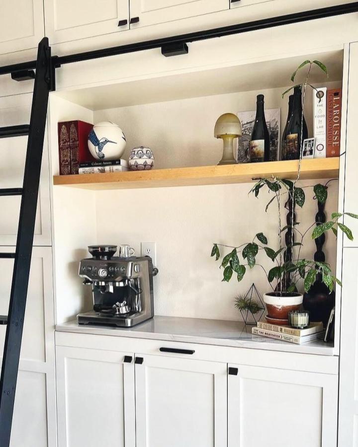 White built-in coffee bar from @braveelement. Wood shelf, black hardware, espresso machine, and trailing plants style this IKEA coffee station.