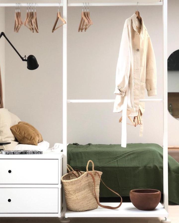 White Elvarli bedroom divider from @lenka_pelc. Open shelving separates a bed with green bedding, wood hangers, and woven storage.