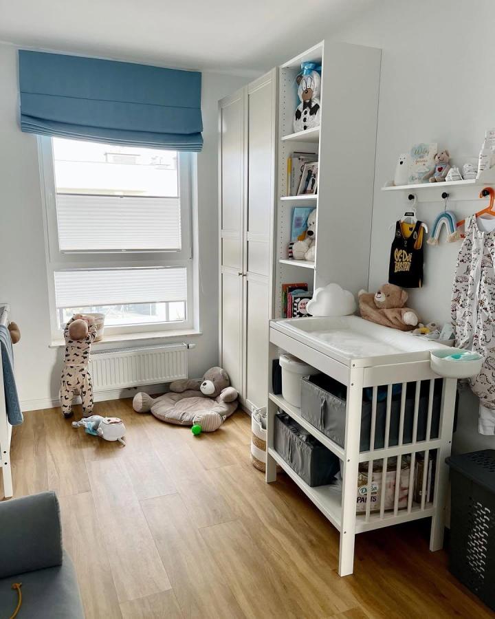 White PAX-style nursery wardrobe from @emilie_dob. Blue Roman shade, changing table, open shelves, and cuddly toys.