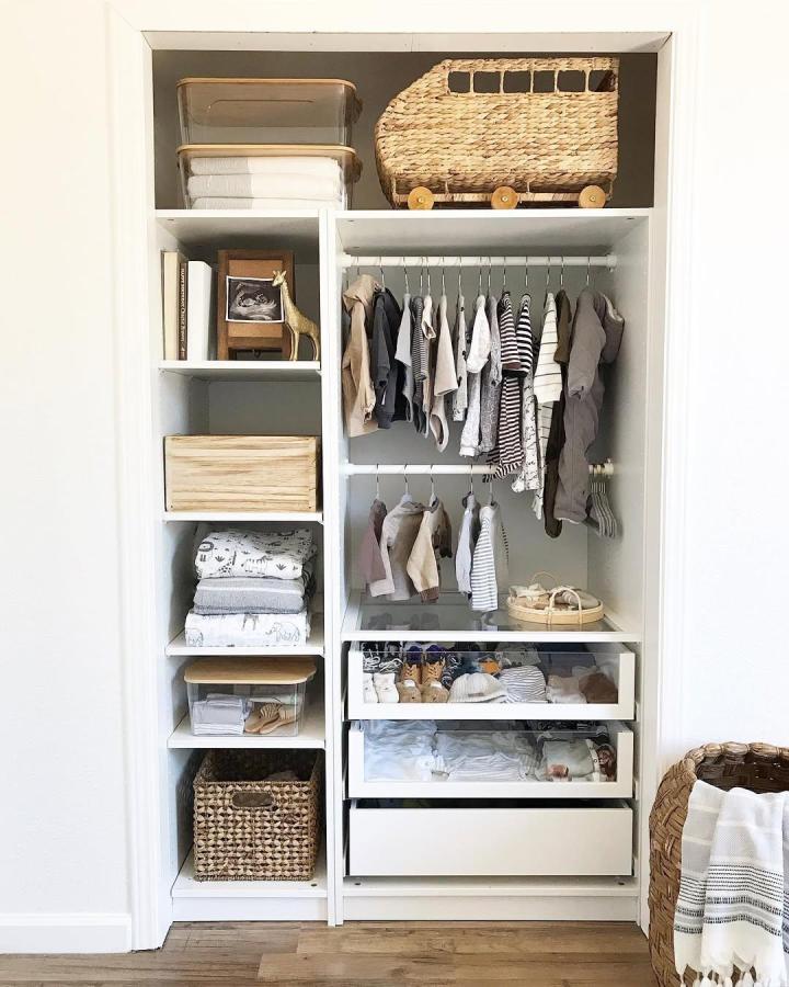 Natural woven IKEA PAX nursery wardrobe from @livandmarket. White shelving, striped clothes, baskets, and organized drawers.