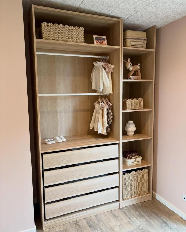 Warm oak-toned PAX nursery wardrobe from @susannalamhauge. Scalloped rattan baskets, drawers, tiny clothes, and open shelving.
