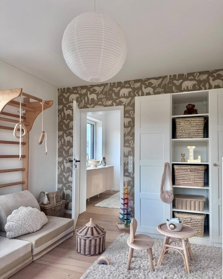Taupe-gray animal wallpaper nursery storage from @_sonjas_picturebook. White Pax wardrobe with rattan baskets and pale wood play furniture.