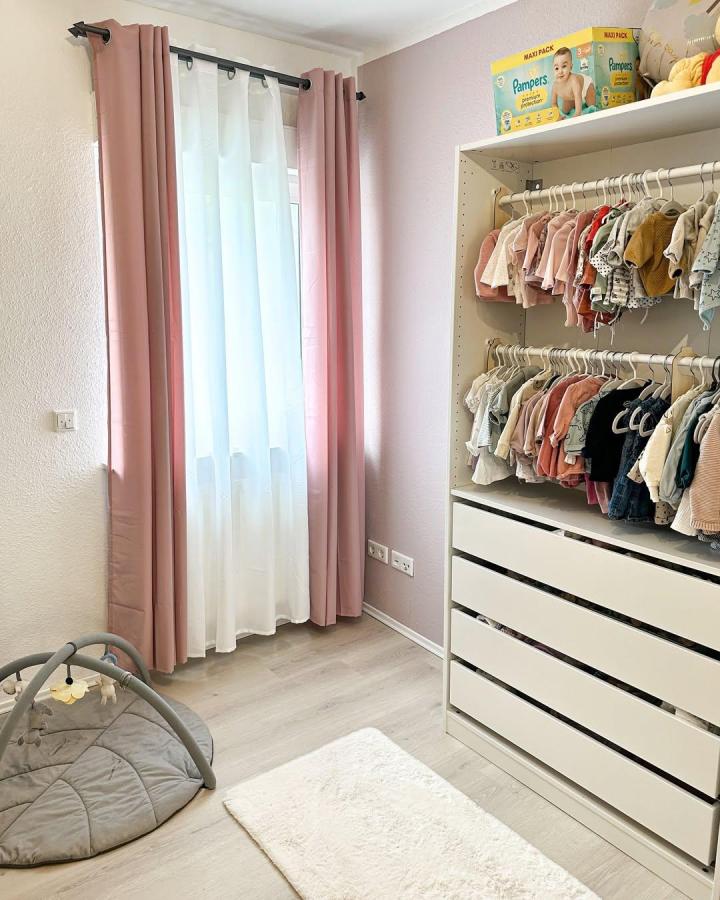 Soft pink and white IKEA PAX nursery wardrobe from @cococreamy3994. Neatly arranged baby clothes and drawers.